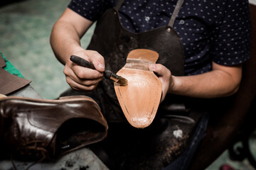 Obraz premium Male cobbler sitting at his shop and repairing man's shoe, brushing glue over sole. Vintage look.