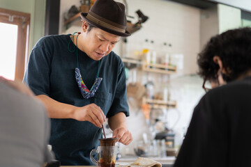 A young Asian barista wears a neatly brown hat to make drinks for customers who order drinks in the coffee shop.