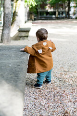 A year and a half old baby taking his first steps in a park with a loose stone floor