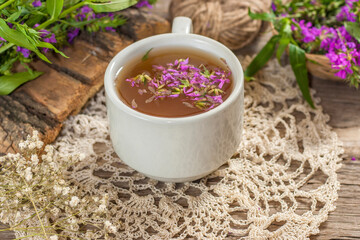 Fireweed is a healthy herbal tea. Mug of traditional russian drink ivan tea on a wooden background with fireweed flowers