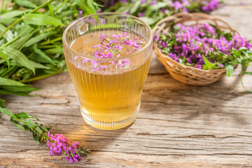 Fireweed is a healthy herbal tea. Mug of traditional russian drink ivan tea on a wooden background with fireweed flowers