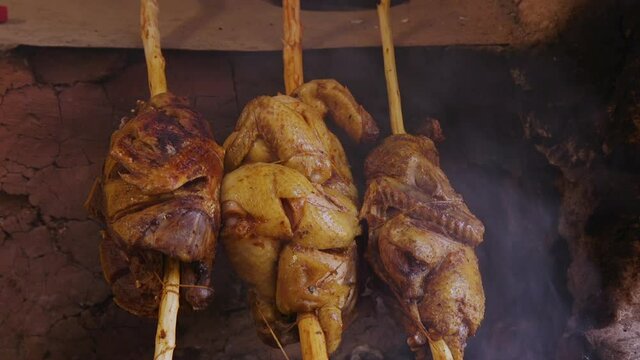 A duck and two chickens cooking over a smokey fire. Close Up.