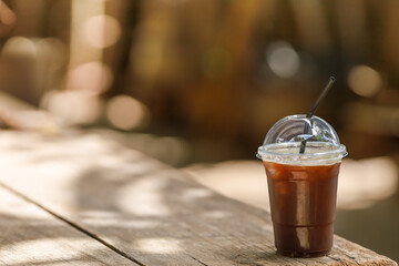 Closeup of takeaway plastic cup of iced black coffee Americano on wooden table with copy space.