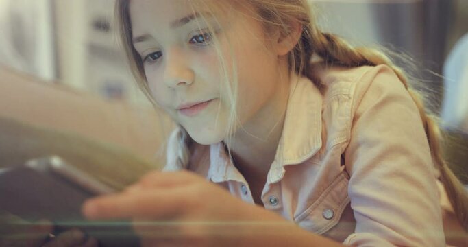 Curious preschool girl using digital tablet lying on sofa. A small child keep an electronic device surfing the Internet and play games at home.