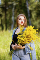 Portrait of a young girl with a bouquet of wildflowers against forest or park on blurred background.. Shallow focus.