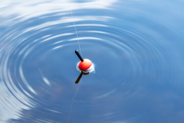 Fishing float in the blue water. A bobber floats on the water surface of the lake making circles in the water. Top view. - 366117404