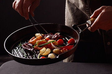 Chef cooks seafood, shrimp in a pan with vegetables.