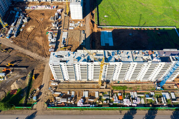 Construction site of a residential building. Construction cranes work along the building on crane tracks, and construction materials are stored around the building. The view from the top. 