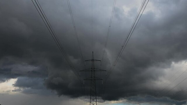 Time lapse summer dark storm clouds moving over forest and transmission electricity steel pylon tower. Zoom in