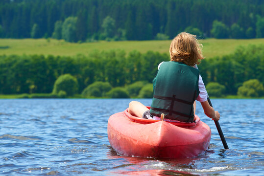 Active happy boy in summer holiday. Teenage school boy having fun enjoying adventurous experience kayaking on lake on a sunny day during summer vacation.
