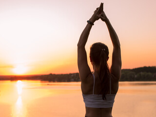 Beautiful athletic girl doing yoga outdoors at sunset. She meditates and does the practice of purification, healing. Girl promotes a sporty lifestyle.