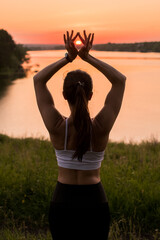 Beautiful athletic girl doing yoga outdoors at sunset. She meditates and does the practice of purification, healing. Girl promotes a sporty lifestyle.