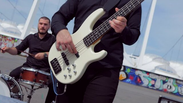 The guy plays cool bass guitar. Music band plays on the background of the stadium. Professional musician.