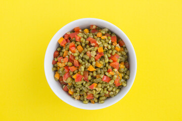 Mung beans with vegetables in the white bowl in the center of the yellow background. Top view. Closeup.