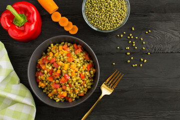 Mung beans with vegetables in the bowl on  black wooden the  background. Top view. Copy space.