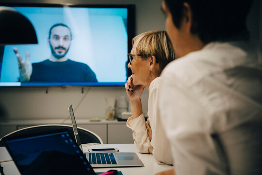 Colleagues listening to businessman during video conference in board room at office