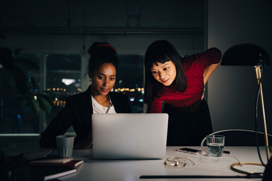 Confident female business colleagues discussing over laptop while working late at creative office