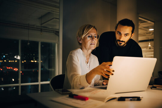 Businessman listening to mature businesswoman during meeting at late night in office