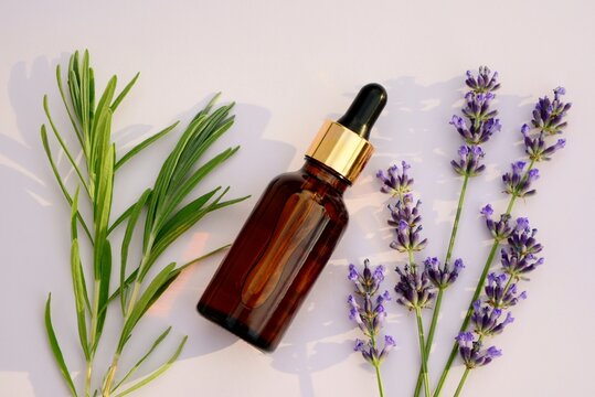  Lavender oil in a bottle and lavender flowers on light background top view