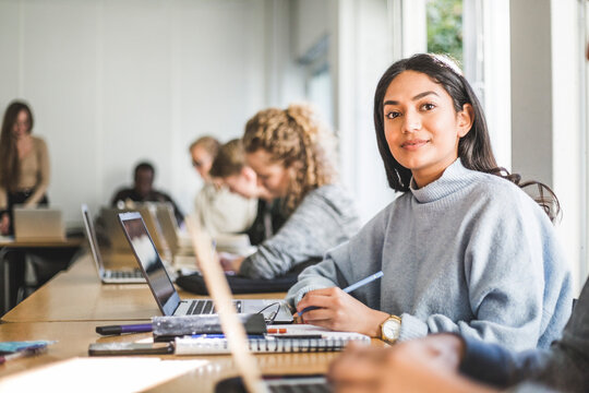 Portrait of confident young woman at desk in classroom