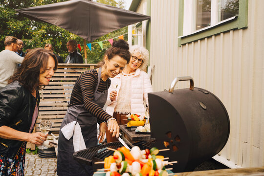 Smiling senior female friends barbecuing dinner at back yard during garden party