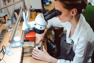 Diligent jeweler working on microscope at her workbench