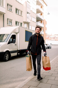 Confident Young Delivery Man Carrying Grocery Bags On Street In City