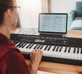 A woman is taking piano lessons online. Education at home. Music notes on screen, hands close up