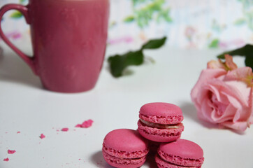 Three pink almond macaroons and mug with coffee on a white wooden background next to a pale pink rose. good morning concept