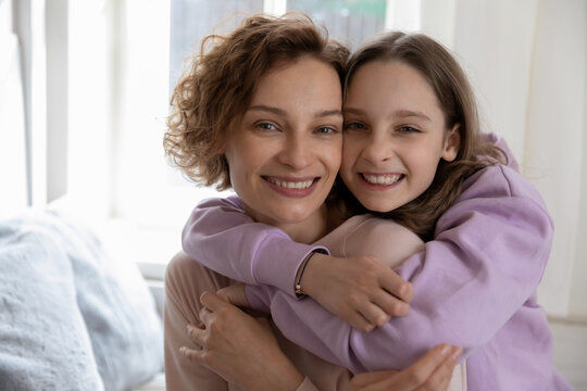 Head shot portrait smiling teenage daughter hugging mother from back, overjoyed beautiful mum piggy backing teenager girl, looking at camera, happy family posing for photo together