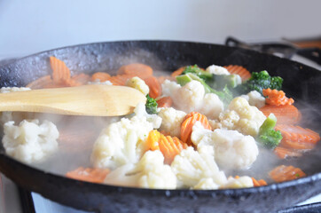 Mixed fresh vegetables in a skillet, fried stewed vegetables in a pan with a wooden spoon,...
