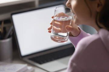 Close up thirsty teenage girl drinking pure mineral water, holding glass, teenager sitting at table...