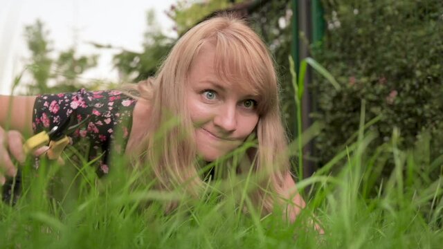 Crazy Pedantic Woman Cutting Green Grass With Scissors In Private Yard. Meticulous Female Worker Mowing High Grass Near House. Housewife With Secateurs In Garden. Outdoor Seasonal Household Works.