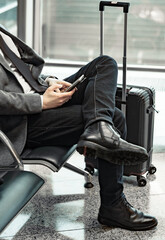 man waiting for his flight at the airport and looking at a mobile phone