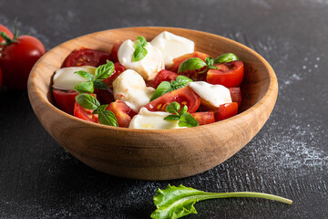 Homemade caprese salad in wooden bowl on black background close up. Traditional Italian dish. Healthy diet food concept.