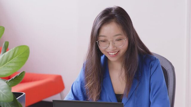 A young Asian woman is making a video call to relatives and friends with a laptop at home. Concept of technology, modern generation, family, connection, authenticity. - slow motion