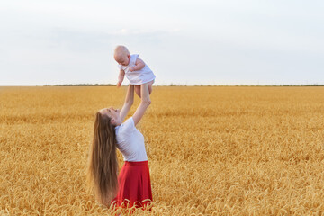 Young beautiful mother and baby playing in wheat field. Mom raised baby