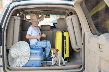 Happy boy in a cowboy hat and puppy jack russell terrier travel by car. A child and a funny little dog are sitting in the trunk and are ready for summer vacation. Independent travel. Best friends.