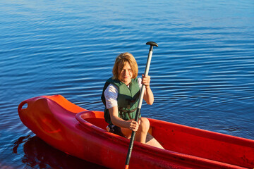 Active happy boy in summer holiday. Teenage school boy having fun enjoying adventurous experience kayaking on lake on a sunny day during summer vacation.
