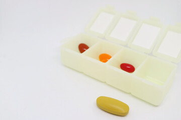 Closeup a Yellow Pill Isolated on White Background with Blurry Pill Organizer Case in the Backdrop