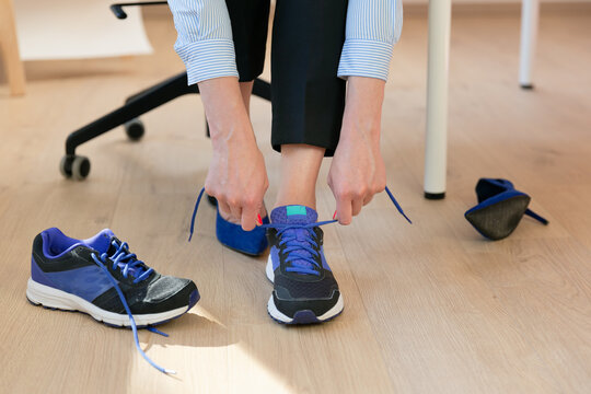 Woman Changing High Heels, Office Shoes After Working Day While Sitting On The Chair, Ready To Take A Walk Or Run	