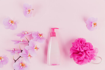 Plastic dispenser bottle with cosmetic soap, shampoo or shower gel, pink sponge and purple orchid flowers on pink background. Spa and wellness concept