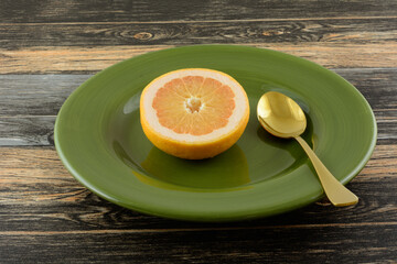 Breakfast plate of fresh raw grapefruit half on green plate with golden spoon