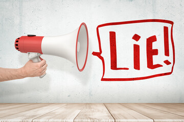 Man's hand holding red and white megaphone against grungy white wall with big speech bubble that says 'Lie'