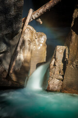 Fototapeta na wymiar Bright waterfall rushing between rocks and branches slow shutter speed