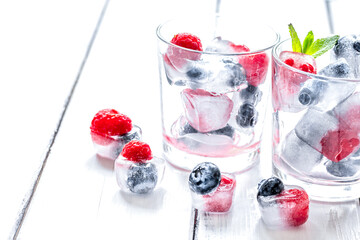 Ice cubes with blueberry and raspberry in glass on wooden table