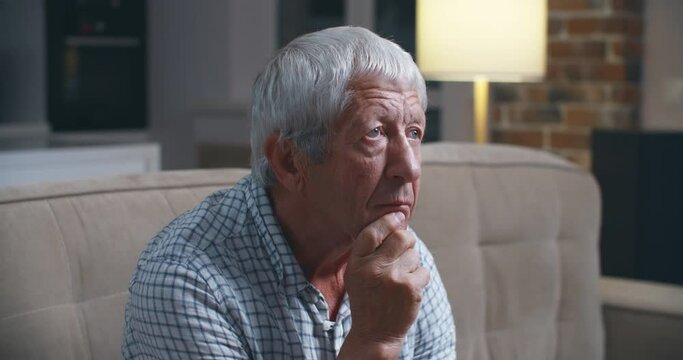 Grey haired old man sit on couch in living room alone, lost in sad pessimistic thoughts related to senile disease, mental disorder memory loss or dementia. Life troubles and lonely 80s person concept.