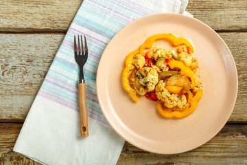 Vegetable stew on a beige plate on a napkin with a fork on a wooden table.