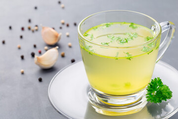 Chicken broth in  glass cup with chopped parsley, horizontal, closeup