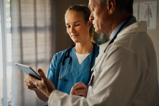 Male doctor discussing patients results on digital tablet with female nurse in scrubs